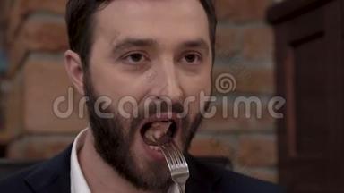一个留胡子的男人的特写`他的脸在一家精致的餐厅里把一块食物放进嘴里。